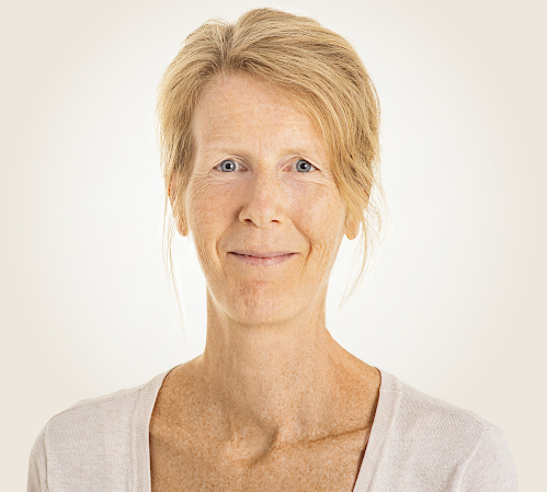 Eine lächelnde Frau mit blauen Augen und hochgesteckten blonden Haaren, die Natürlichkeit und Authentizität ausstrahlt.